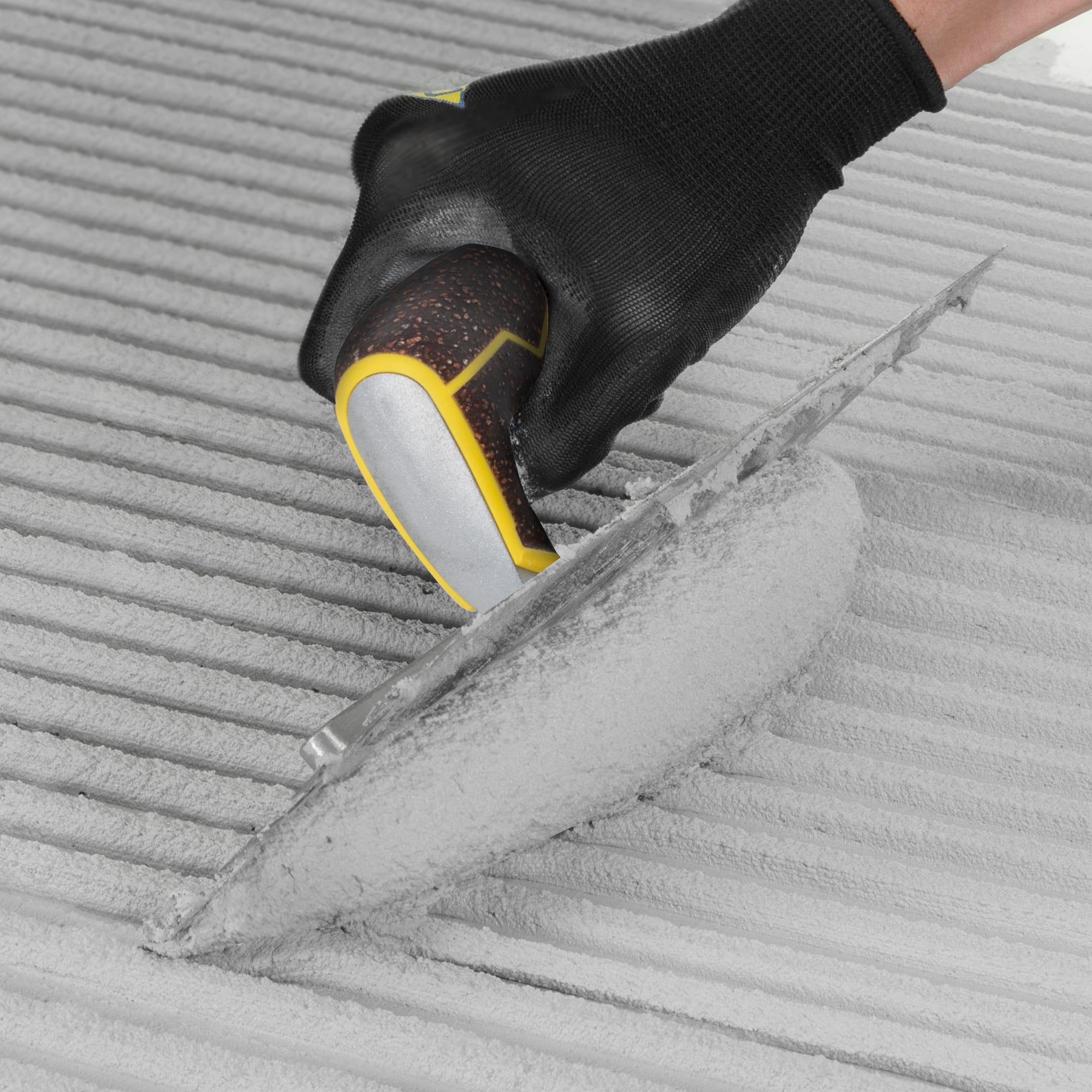 Notched trowel combing thinset mortar into ridges on a tiled surface, gloved hand visible.
