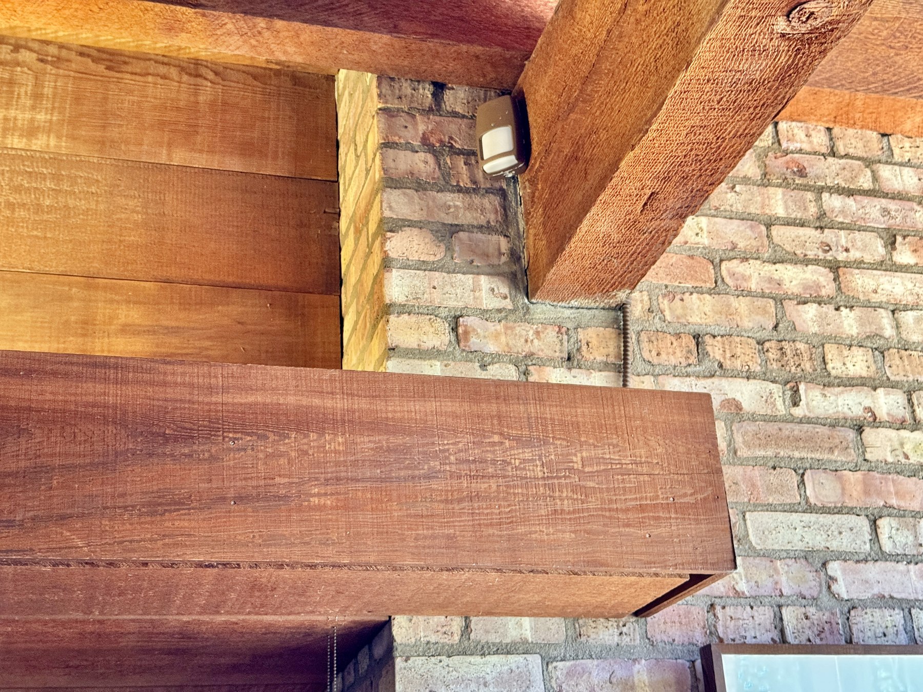 A real close-up of a wood ceiling beam meeting a brick fireplace wall, showing genuine texture variety