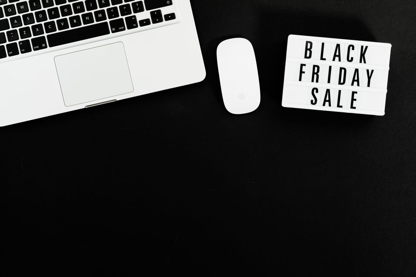 Laptop beside a lit "Black Friday Sale" sign on a dark desk