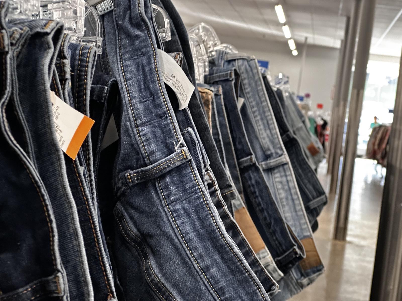 A rack of secondhand denim jeans at a thrift store, a real photograph, referencing the deadstock and reclaimed materials Ahluwalia builds collections from.