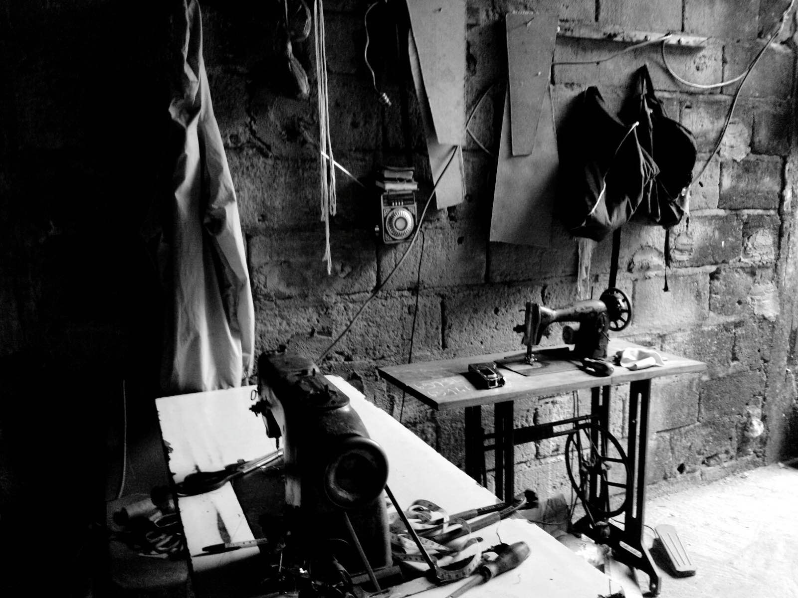 A small sewing atelier with a tailor working at a table, a real photograph, referencing Studio Nicholson's fabric-first design approach.