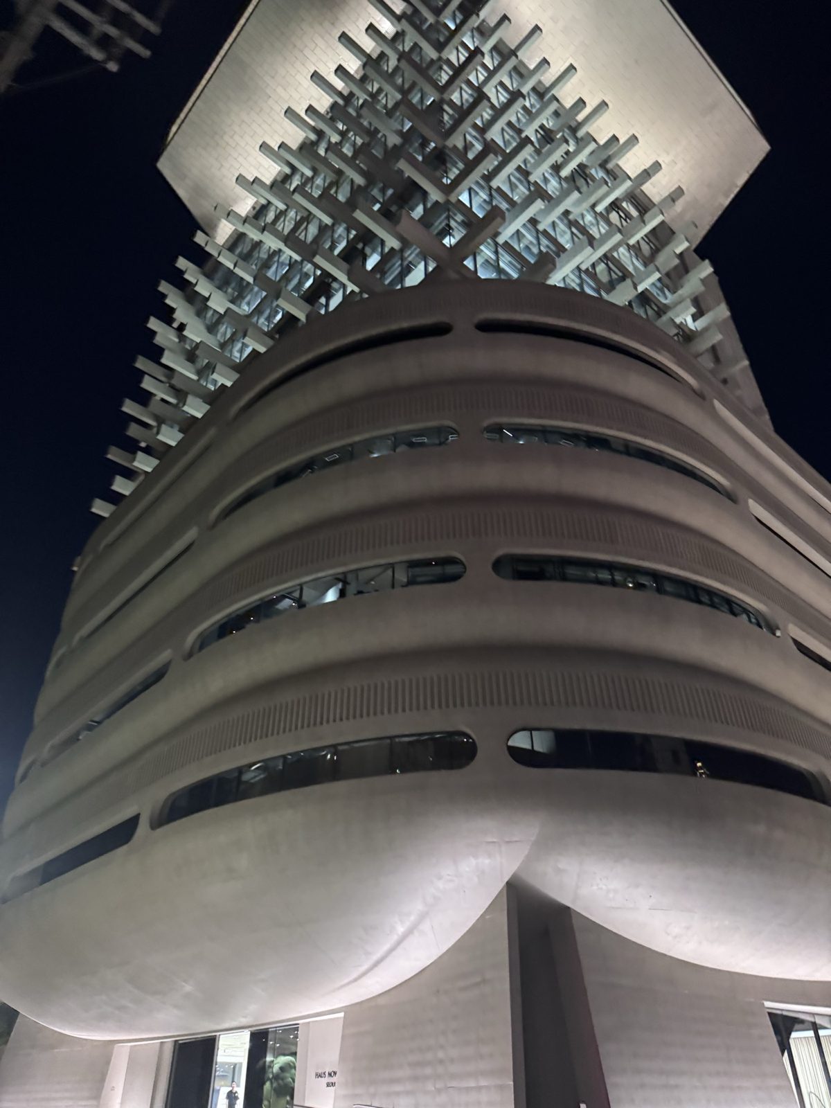 The curved, banded facade of Haus Nowhere Seoul lit from below at night, a lattice crown on top.