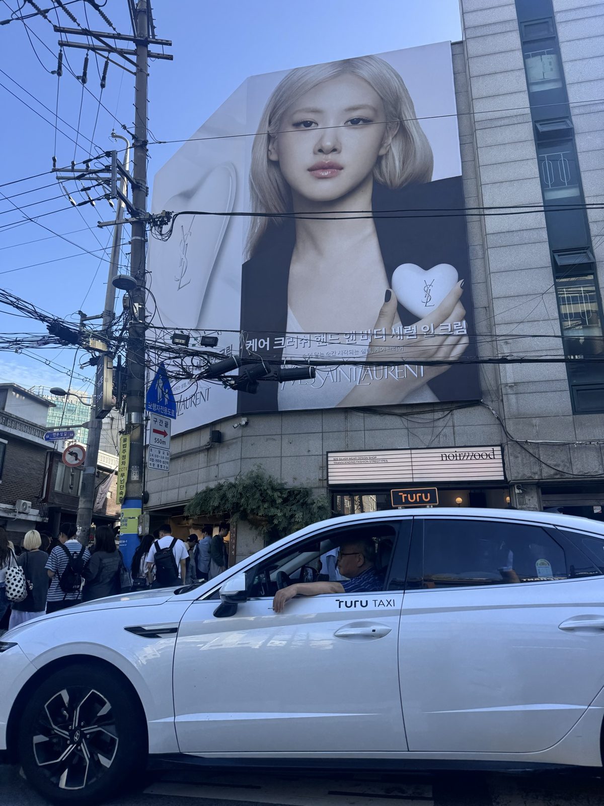 A Seongsu street with a large fashion billboard above parked cars and overhead wires.