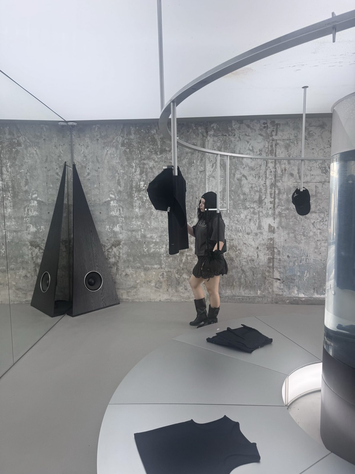 A gallery-like Seongsu store interior with raw concrete walls, black garments hanging from a curved rail and a tall pyramid sculpture.