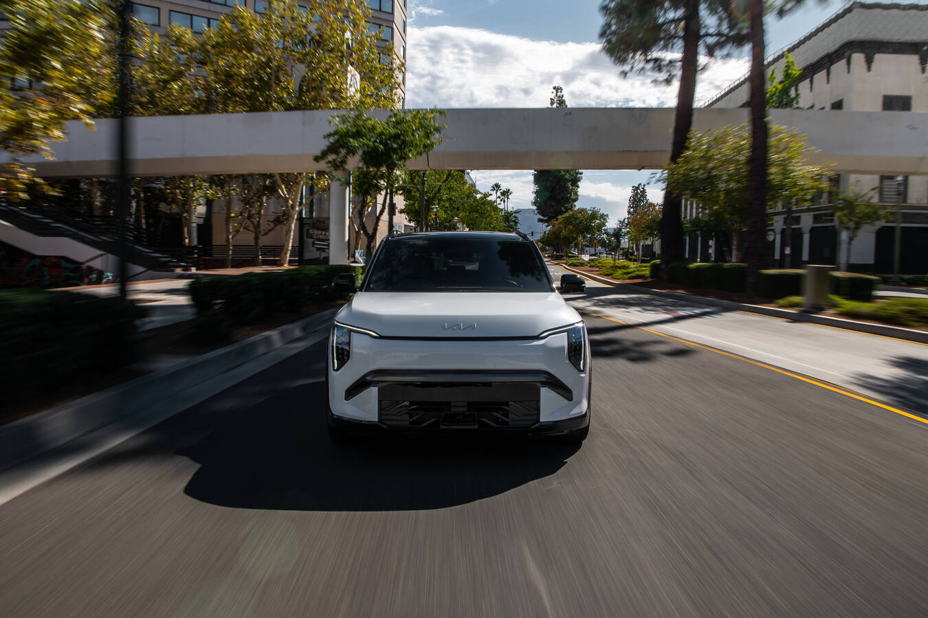 2027 Kia EV3 driving toward the camera under a pedestrian overpass, official Kia press photography.