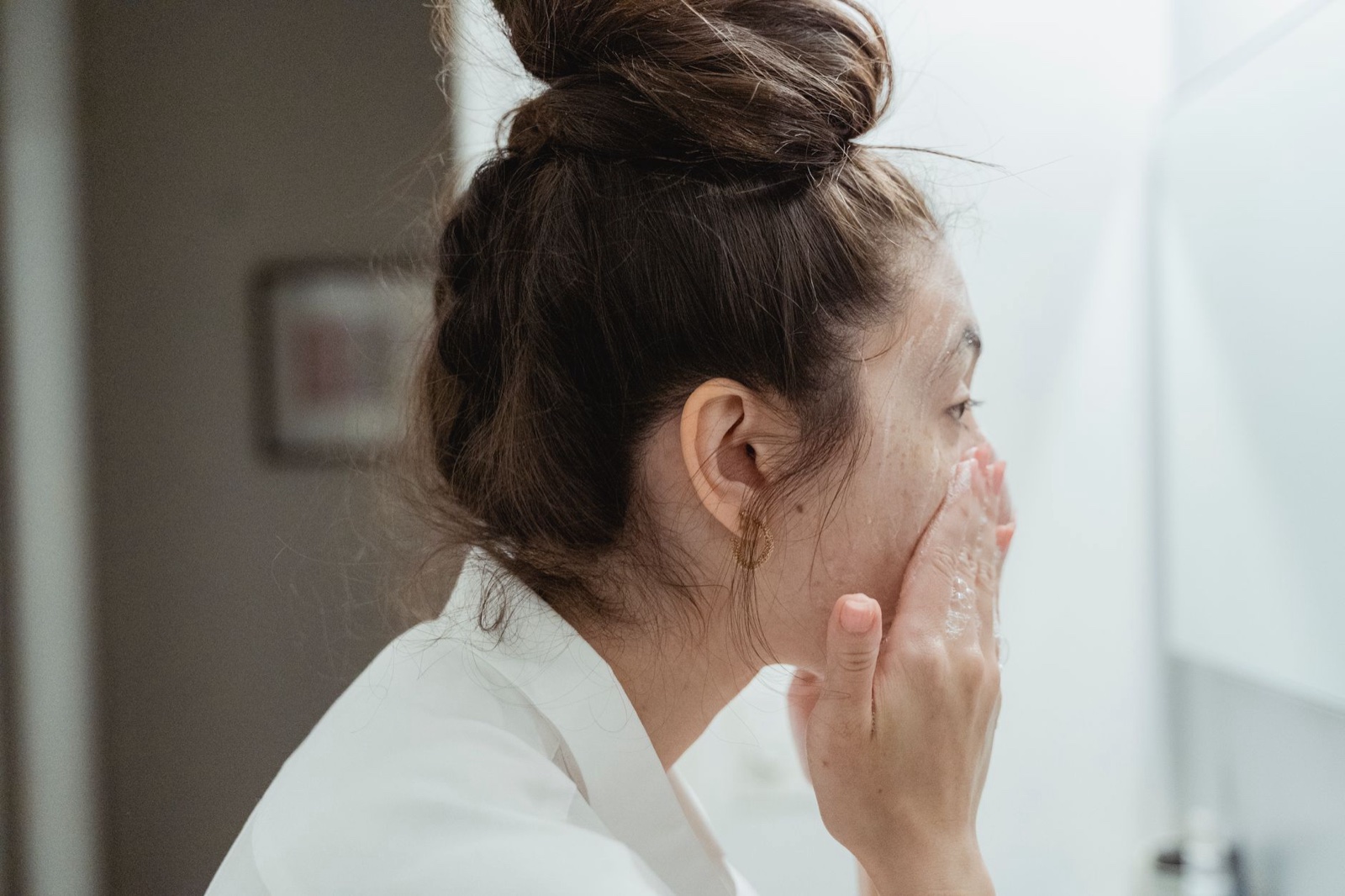 A woman washing her face at a bathroom basin, seen from the side.