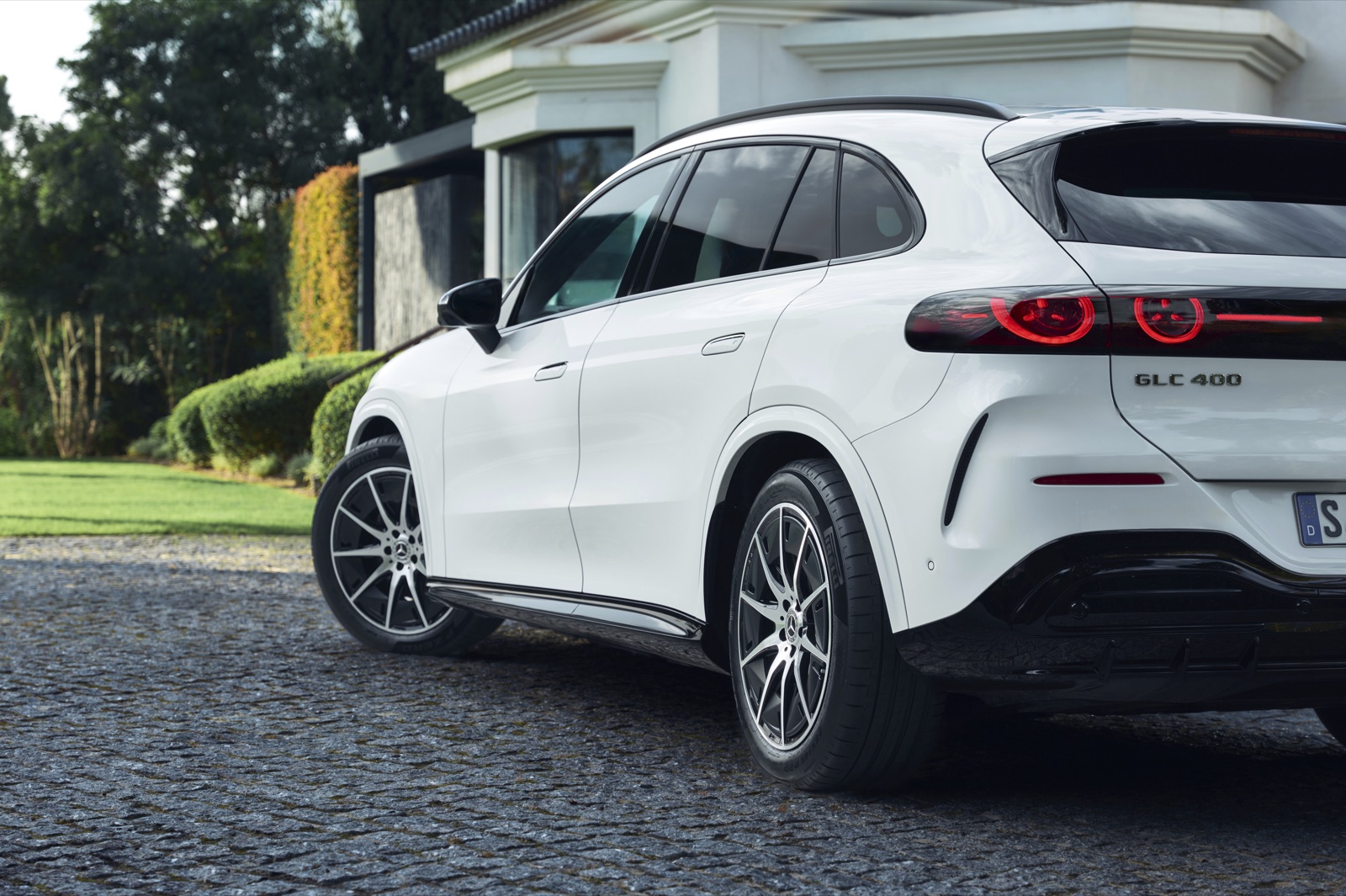 Rear three-quarter view of a white Mercedes GLC 400 with illuminated rear light rings, parked on cobbles.