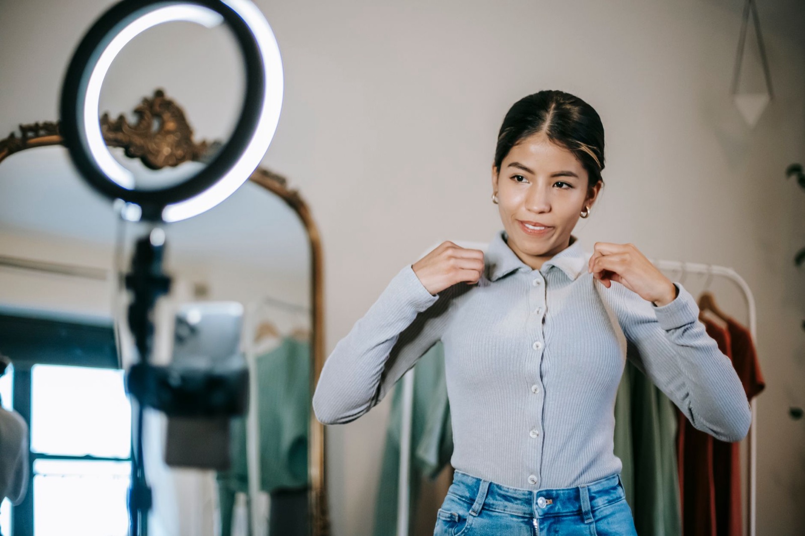 A woman standing in front of a mirror holding a phone, filming herself.