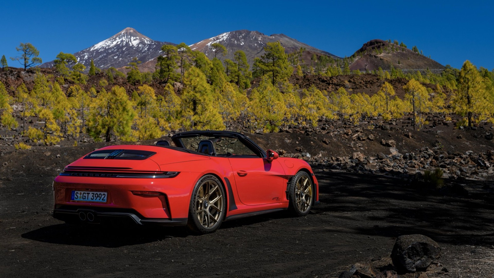 A red Porsche 911 GT3 S/C parked on volcanic ground with Mount Teide behind it, rear three-quarter view.