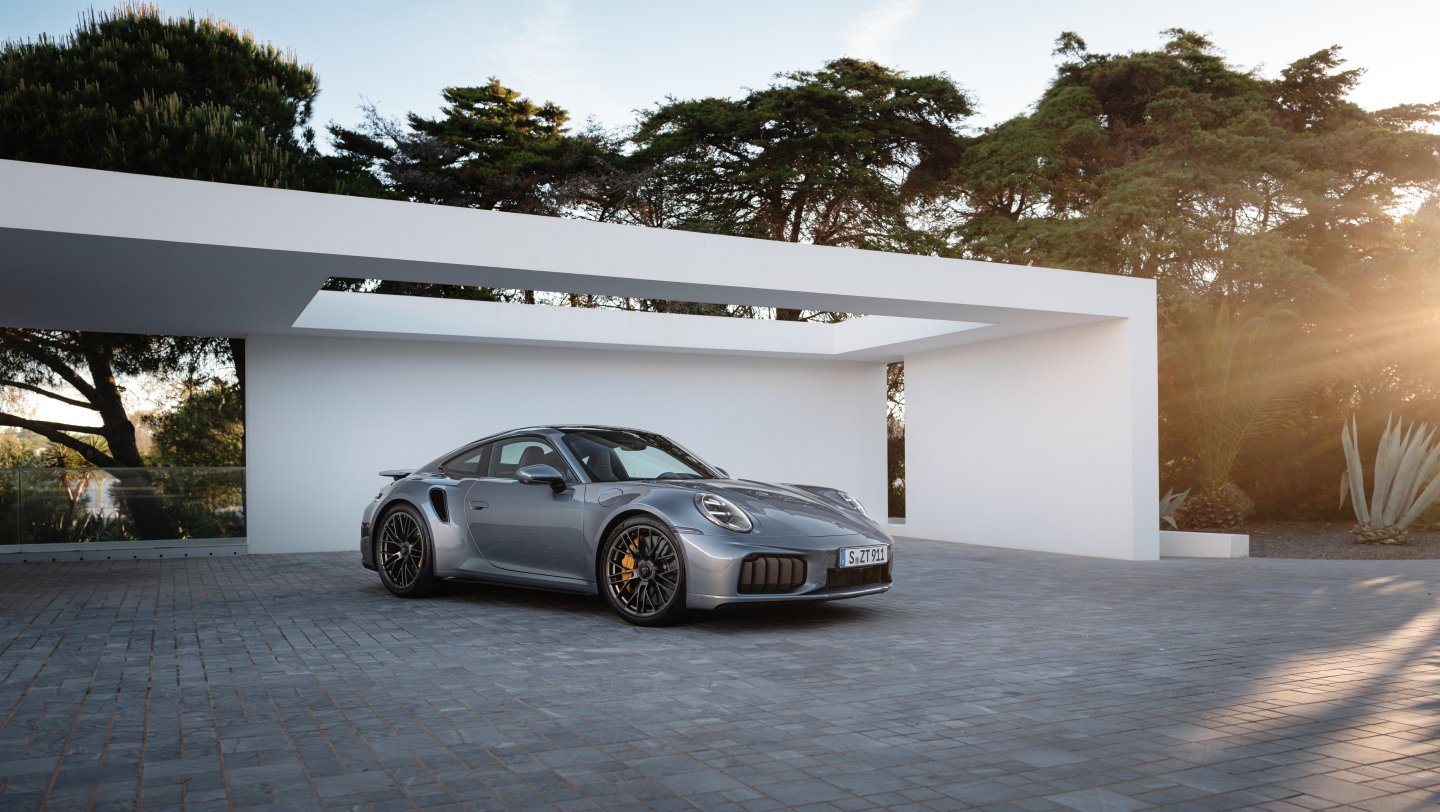 2026 Porsche 911 Turbo S in silver, parked in front of a modern white building.