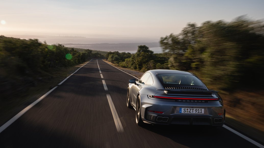 911 Turbo S driving away on a coastal road at sunset.