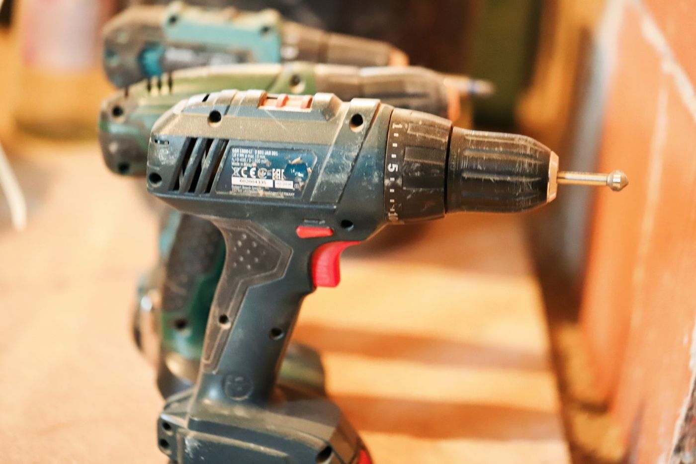 Close-up of several cordless drills of different brands lined up on a workbench