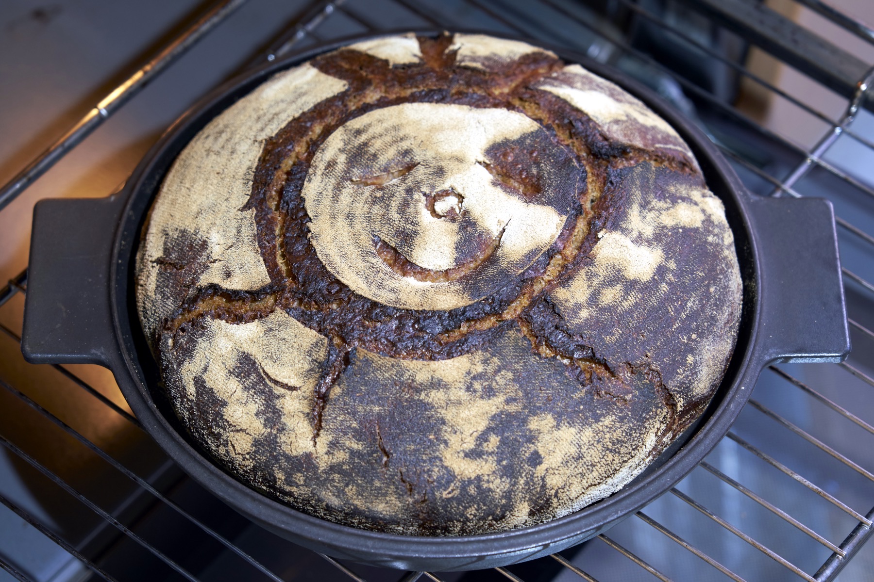 A baked sourdough loaf with a scored top, cooling in a Dutch oven, a real photograph.
