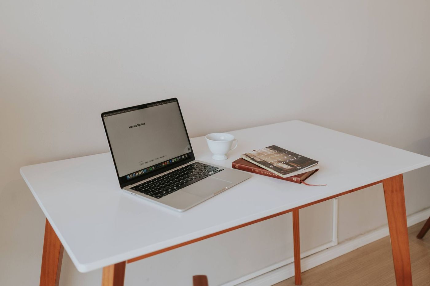 Laptop open on a white desk with a cup and a book