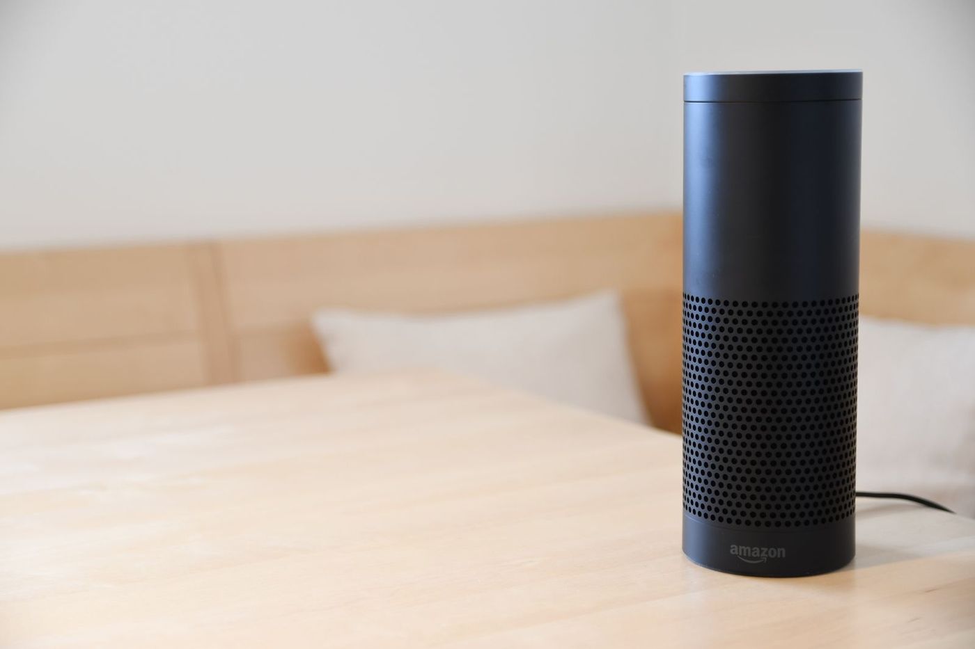 Black cylindrical smart speaker on a light wooden table