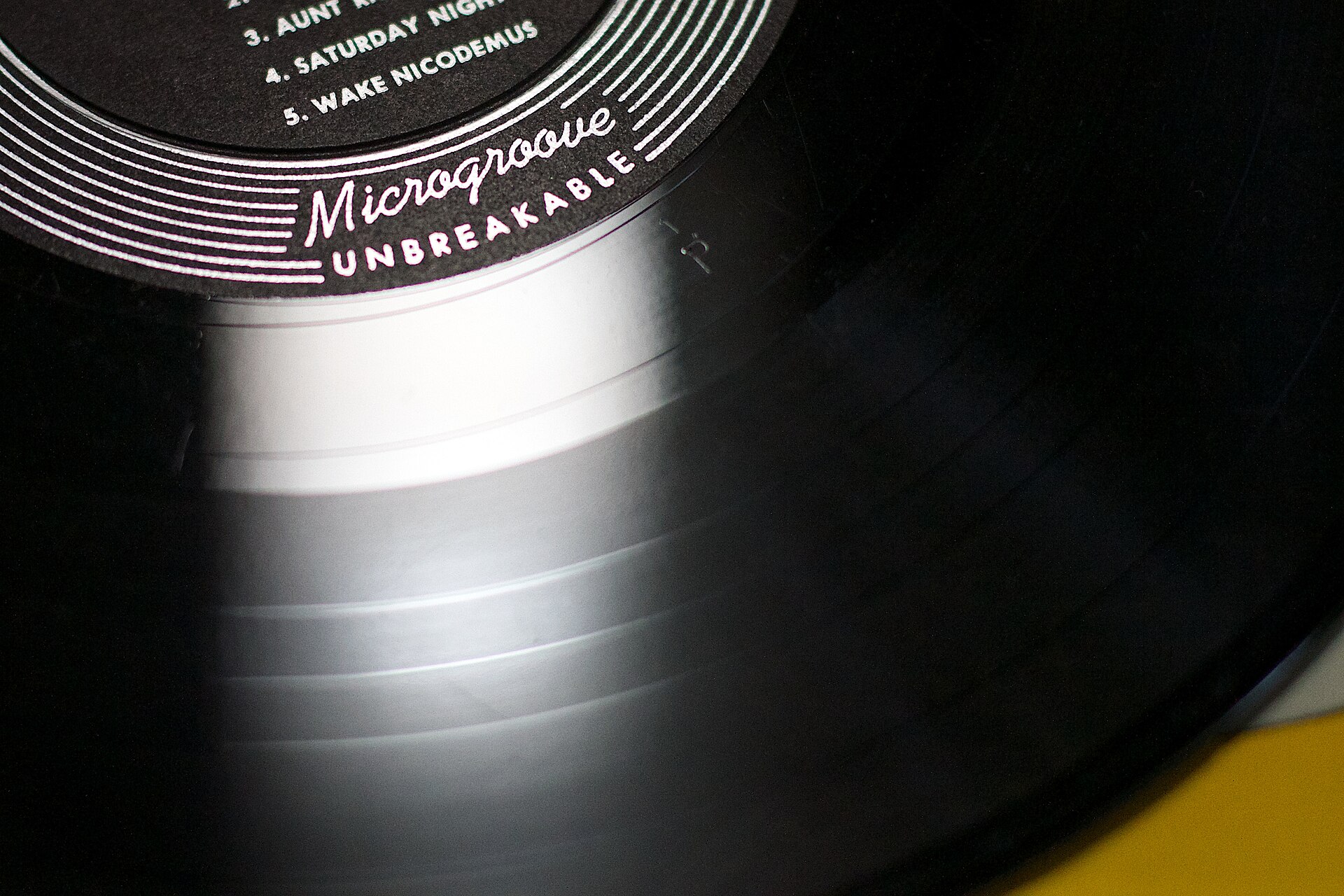 Extreme close-up of a vinyl record's grooves and label, reading Microgroove Unbreakable, real photograph.