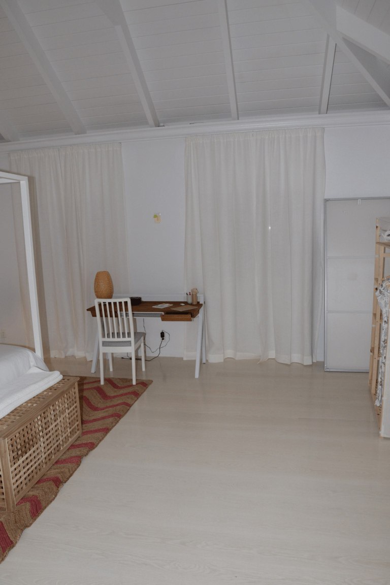 A real minimalist bedroom with white walls, light wood flooring, and a simple wooden desk