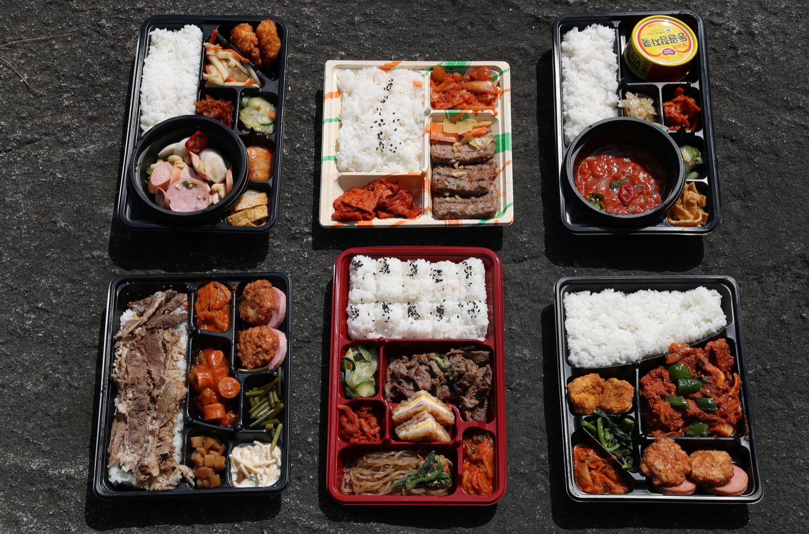 Six Korean convenience-store lunch boxes (dosirak) arranged from above, showing rice, meat, and side dishes.