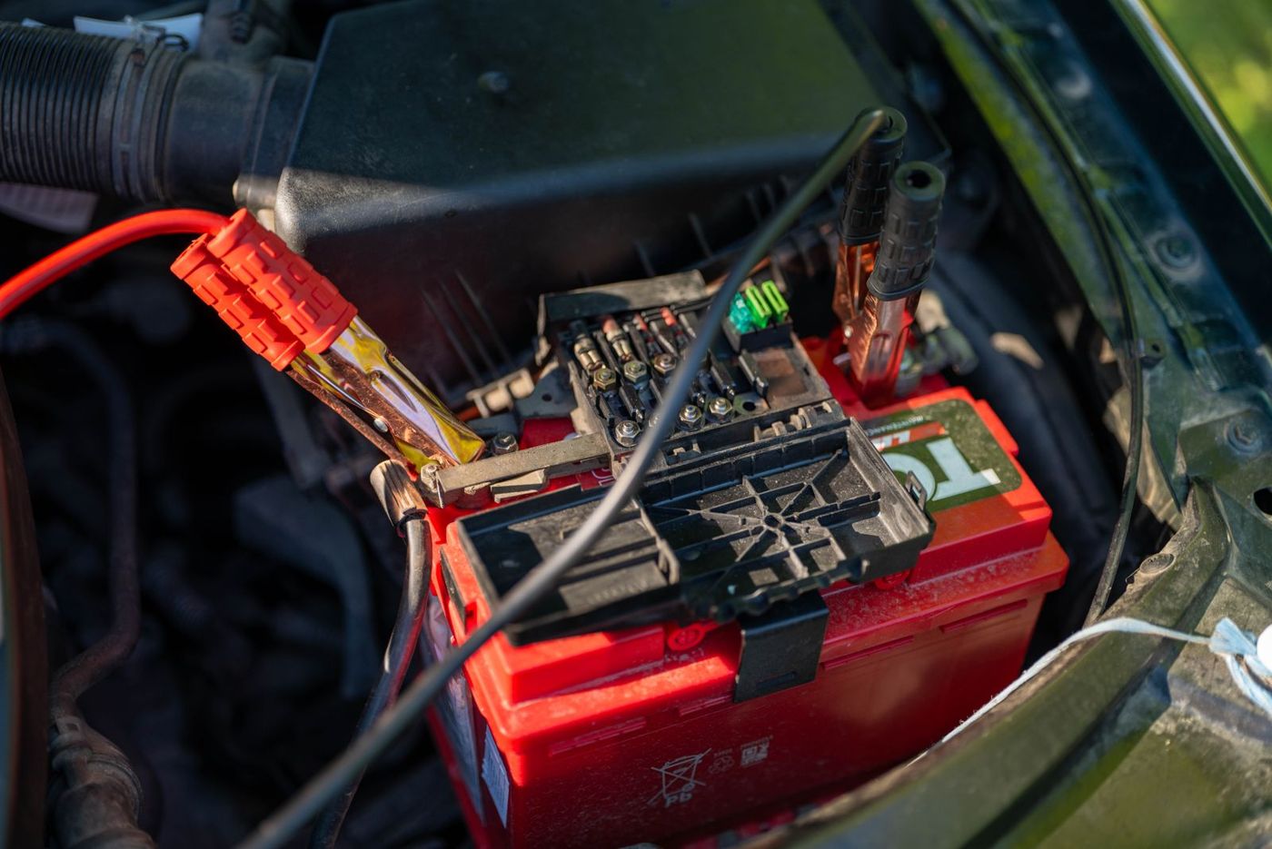 Jumper cable clamps attached to a car battery under the hood