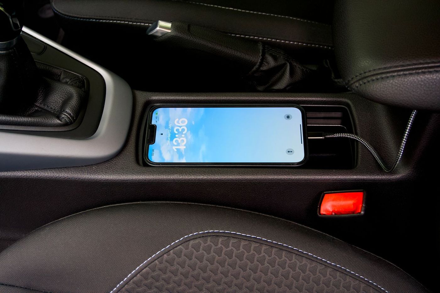 A smartphone charging on a cable in a car center console