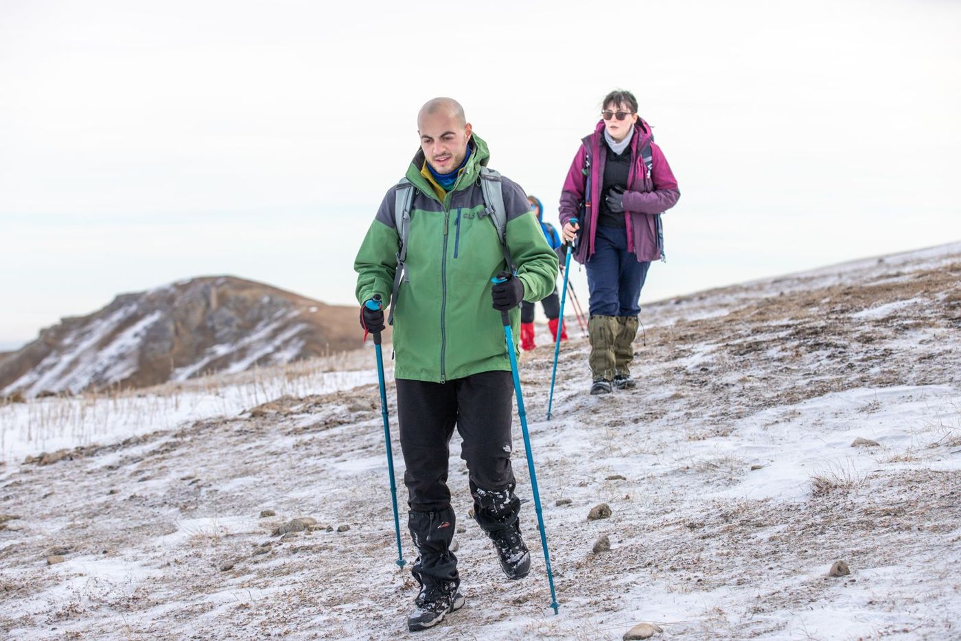 Hikers using trekking poles on a patchy snow slope