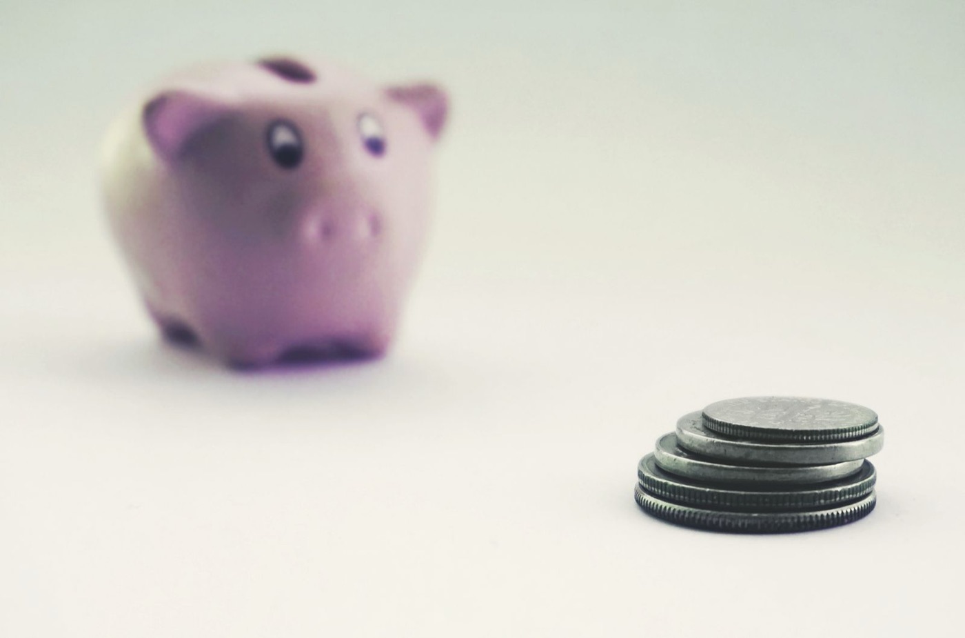 Coins stacked next to a piggy bank, a real stock photograph representing a no-spend savings challenge.