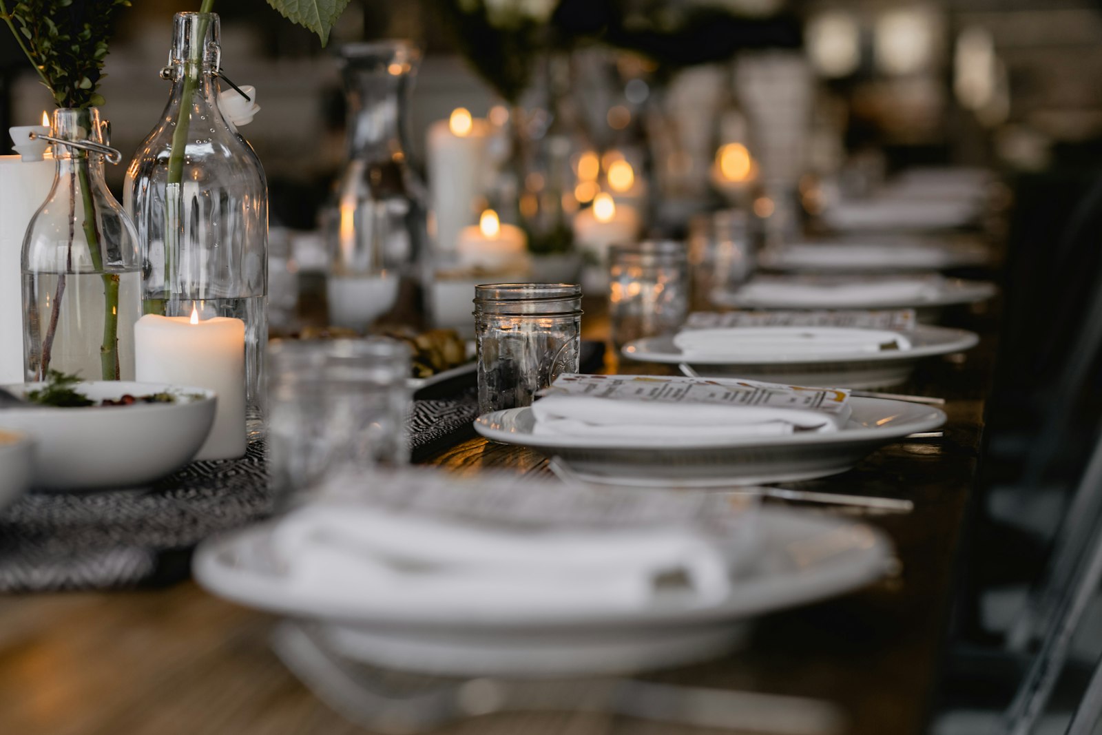A formal dining table set with white plates, candles, and glass bottles